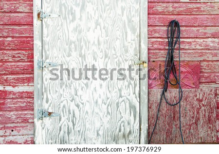 The side of an old red shed with an extension cord, white plywood door and tin ceiling patch