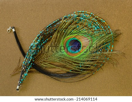 A seed bead necklace in turquoise and gold with a peacock feather
