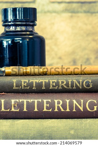 A vintage bottle of ink, fountain pen and lettering books with old fashioned processing look