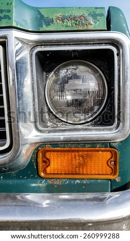 A close up of a headlight and the corner of the bumper on an old abandoned truck