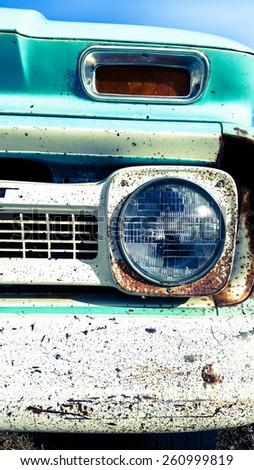 A close up of a headlight and the corner of the bumper on an old abandoned truck