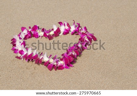 A traditional, Hawaiian lei made of pink and white orchids in a heart shape on a beach in Hawaii