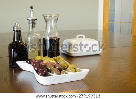 A party tray of mixed olives with a carafe of red wine, and bottles of balsamic vinegar and oil