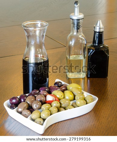 A party tray of mixed olives with a carafe of red wine, and bottles of balsamic vinegar and oil