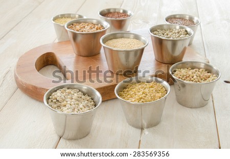 Metal containers with ancient grains with a small cutting board on a rustic white plank  surface