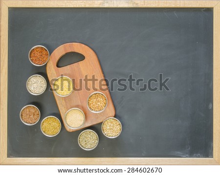 Metal containers with ancient grains with a small cutting board on a blackboard surface