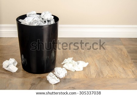 A garbage can with lots of crumpled paper in and around it