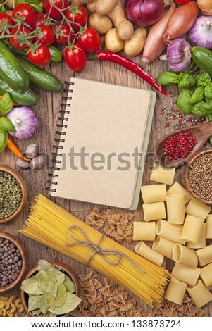 Assortment of fresh vegetables and blank recipe book on a wooden background