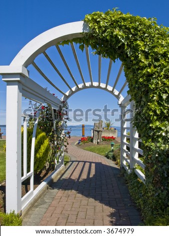 White arch decorated with ivy and flowers framing passage to ocean shore