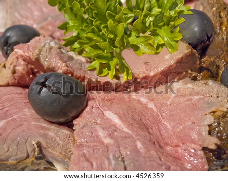 Slices of rare smoked beef decorated with olives and green salad