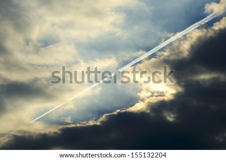 Contrail of a plane over some dark clouds