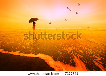 A girl with an umbrella at a beach during sunset / sunrise with birds flying