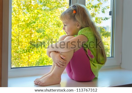 Cheerful girl looking at the beautiful trees outside the window.