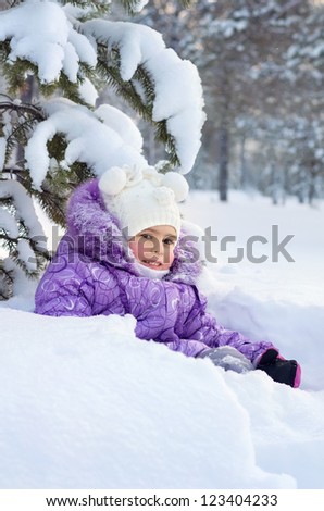 Little girl sits under snow covered branches in the deep snow