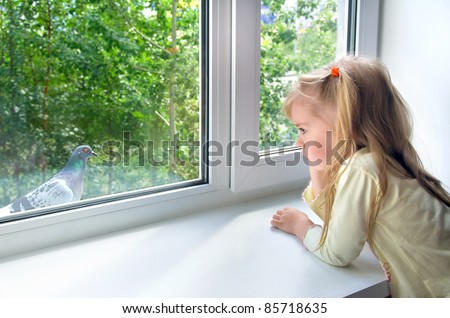 A sad little girl looks at a pigeon outside the window
