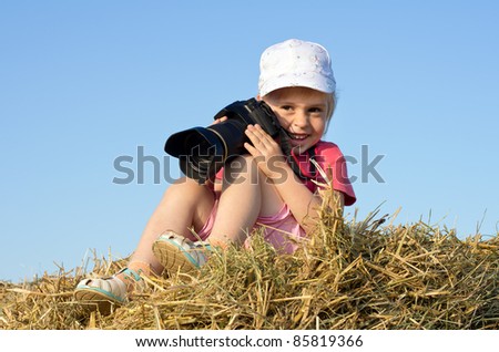 Girl photographer. Little girl sitting on straw with a camera.