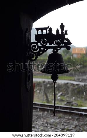 The bell at the train station with metal contour train in the rain
