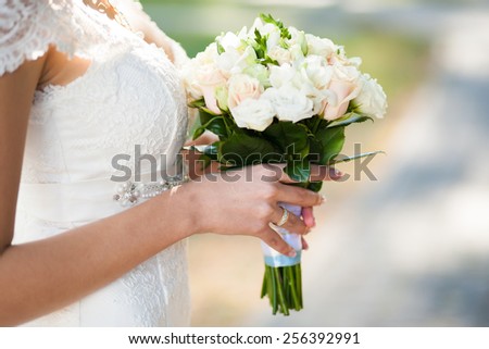 beautiful wedding bouquet of flowers in hands of young bride. weddings. young woman touches flowers with hand. no face. wedding celebration. reception. nature green background. woman alone outdoors