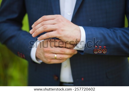 close-up of elegance male hands. man dressed in blue suit and white shirt standing over green nature background. groom or businessman