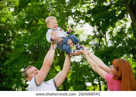 Happy family having fun outdoors in spring garden. Father, mother and child. Family concept. Picnic. Woman, man holding little boy in hands. Laughing, smiling people playing with son