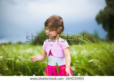 beautiful little girl with wild flowers in green meadow. funny cheerful child playing outdoors.