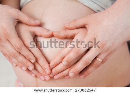 Happy pregnant couple hugging. Man and woman  expecting for childbirth.Portrait of happy family. Making heart shape with hands on belly of pregnant woman. Male and female hands. Unrecognizable people