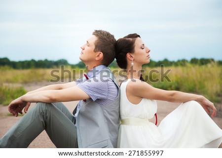 wedding couple sitting on ground. love symbols on pavemant. hearts. people in love. happy bride and groom portraits. man and woman sitting back to back outside on road. newlyweds. wedding day