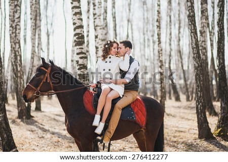 Young woman and man horse-riding. Image of happy wedding couple with purebred horses. Bride and groom riding brown horse.