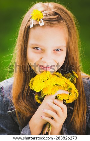 Close up portrait of smiling young girl holding bouquet of flowers in hands. Girl with yellow dandelions. Smiling face of teenager with long hear. Vertical color photo.