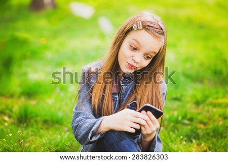 Teen on phone. Young girl on cell phone. Teenager texting or playing games on her phone. Happy smiling kid playing outside over green nature background.