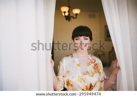 Beautiful Young Woman Looking out From Window. Portrit of Happy Smiling Girl Opening Curtains in Bedroom.
