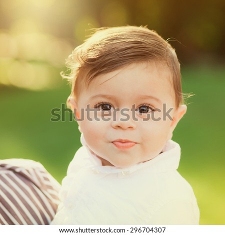 Portrait of beautiful smiling cute baby boy. 8 month old little child playing outside in green summer or spring park.