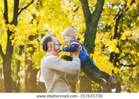 Happy family of two people laughing and playing in autumn wood. Daddy and son at orange trees background on sunny warm fall day.