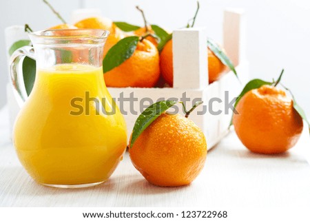 Orange juice in pitcher and tangerines with leaves in wooden box