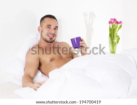 man in bed with naked torso holding a cup