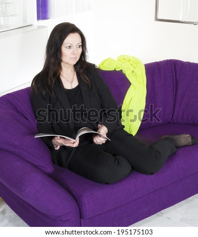 woman in a black suit sitting on purple couch and reading a magazine
