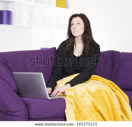woman in black suit sitting on purple couch with a laptop
