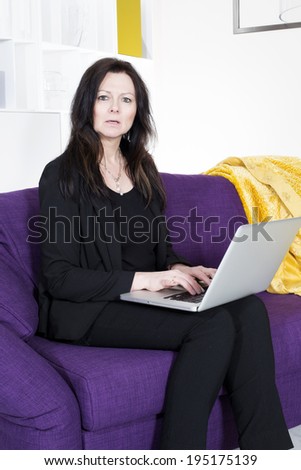 woman in black suit sitting on purple couch with a laptop