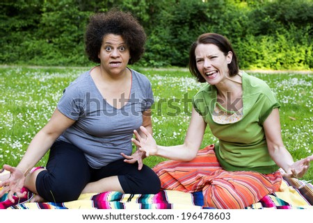 two angry women sitting on blanket in park
