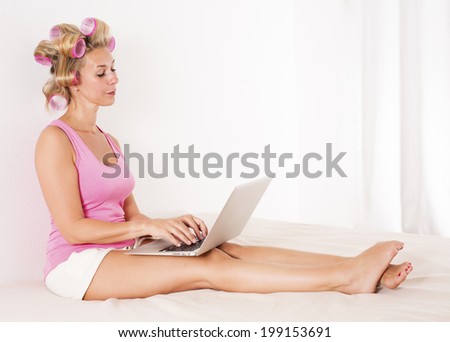 a blond woman with  pink curlers laying in bed with a laptop