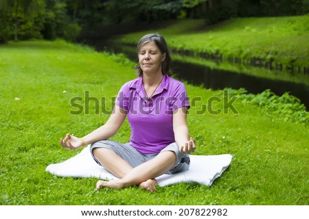 older woman in park by a river doing yoga