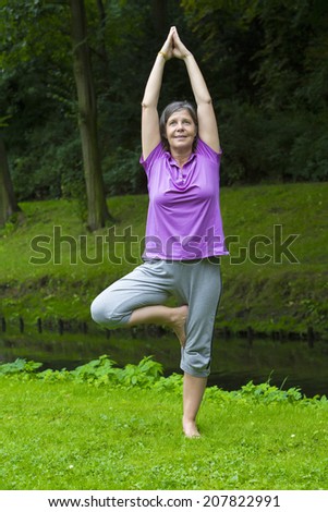older woman in park by a river doing yoga