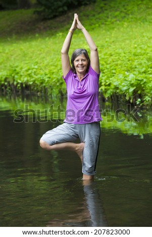 older woman doing yoga in a river