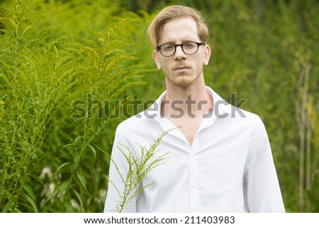 portrait of a young man in a white shirt standing in a park