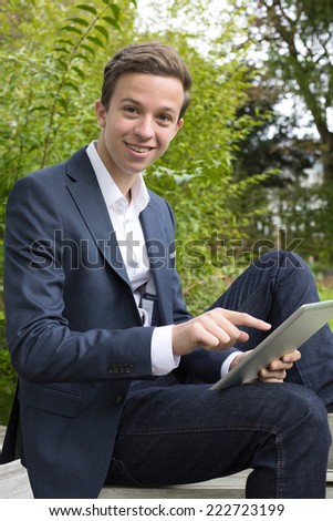 teenager in a suit sitting outside with a tablet
