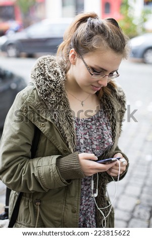 teenage girl standing outside and looking at her phone