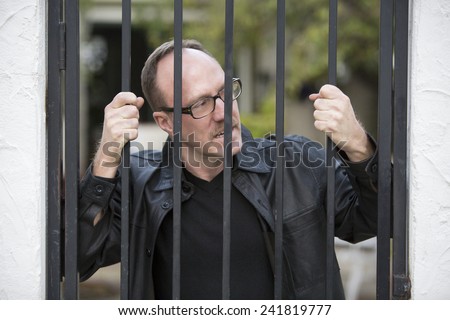 man standing behind iron bars and looking upset