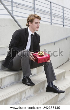 man in suit holding a gift in his hands and sitting on stairs