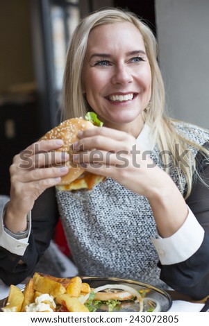 blond woman siting in restaurant with a burger