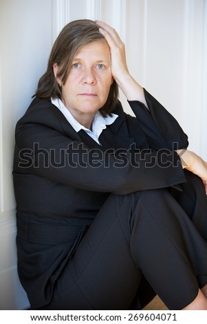 older woman in a suit sitting depressed in a corner